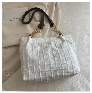 Close-up of white tweed tote bag showing textured fabric and gold chain leather strap