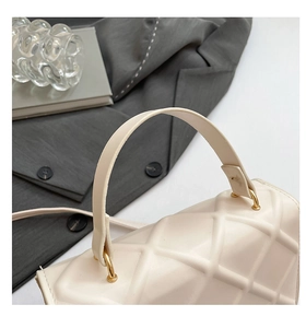 Close-up of cream quilted handbag featuring gold circular hardware and smooth handle detail