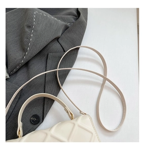 Detail of cream quilted handbag with gold hardware against a grey blazer backdrop