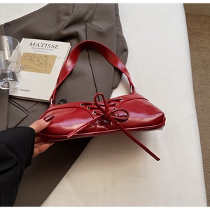 Détail du sac sous le bras en cuir verni rouge avec laçage unique et nœud décoratif