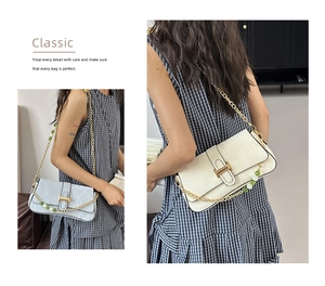 Detail of elegant shoulder bag featuring a gold H-buckle and decorative beaded chain strap
