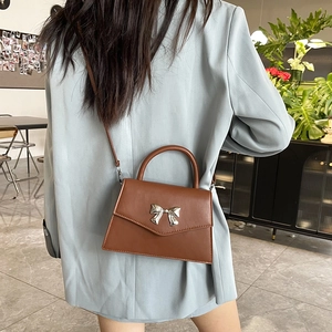 Chic brown leather crossbody bag with silver bow accent shown on model in cafe