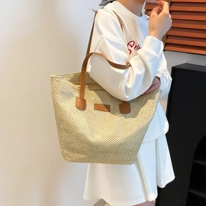 Grand sac cabas en paille avec poignées en cuir marron porté par un mannequin sous lumière douce