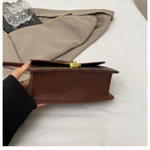 Detailed close-up of retro brown crossbody bag with printed flap and golden metal lock