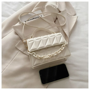 Detailed view of cream quilted handbag with chunky chain next to a smartphone for scale