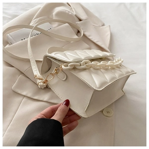 Detail of cream quilted crossbody bag with acrylic chain handle and leather strap