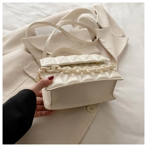 Detailed view of cream quilted crossbody bag with chunky resin chain on a beige blazer