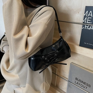 Sac sous le bras en cuir verni noir avec nœud porté à l'épaule sur un pull en maille