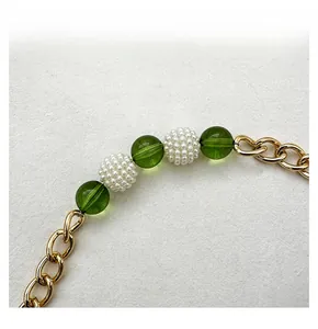 Detail of gold metal chain strap featuring green translucent beads and white pearls