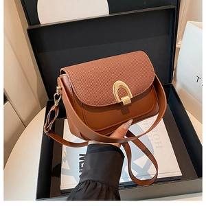 Détail du sac bandoulière marron avec rabat tressé et boucle fer à cheval dorée