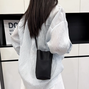 Minimalist black pebble leather vertical crossbody phone bag shown on model for scale