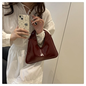 Detailansicht einer glänzenden weinroten Lackledertasche, getragen von einem Modell in Weiß