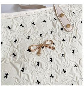 Close-up of cream textured tote with 3D floral pattern and gold metal bow detail