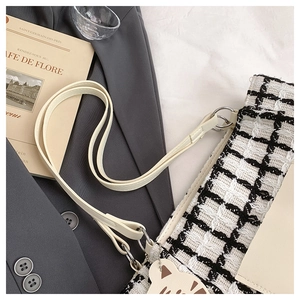 Close-up of black and white checkered tweed shoulder bag with cute cat charm accessory