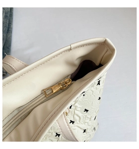 Detail of cream tote bag showing gold zipper, textured surface, and black bow patterns