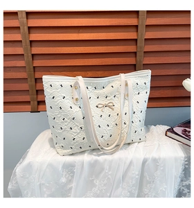 Close-up of quilted white tote bag with black embroidery and golden bow buckle detail