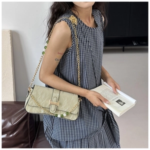 Close-up of sage green pleated baguette bag with gold chain and beaded strap detail