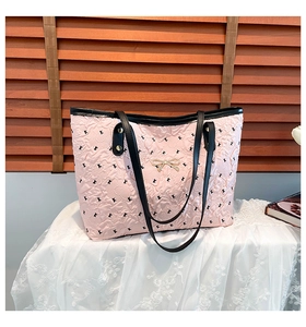 Detail of pink quilted tote bag featuring golden bow accent and black letter patterns