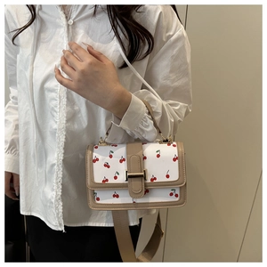Detailed view of white cherry print crossbody bag with khaki leather straps and gold clasp