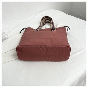 Détail d'un sac cabas en nylon rouge foncé avec poignées rayées et cordon de serrage latéral