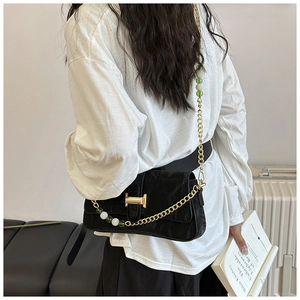 Detail of black crossbody bag with gold chain strap and decorative green and white beads