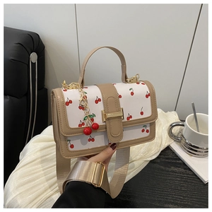 Close-up of white crossbody bag with red cherry print and decorative cherry pendant