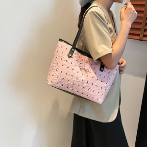 Pink tote bag with black strap and metal bow accessory worn by model against a white wall