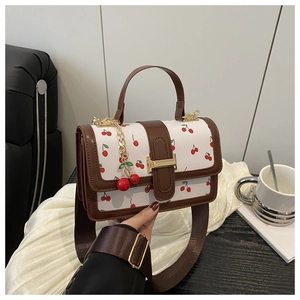 Detail of white cherry print handbag with brown leather trim and wide woven shoulder strap