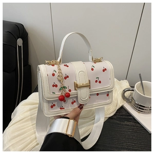 Close-up of white shoulder bag with red cherry prints and golden metallic buckle