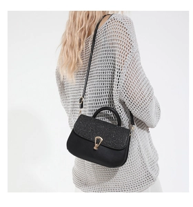 Détail du sac bandoulière noir avec rabat pailleté et boucle dorée porté par un mannequin