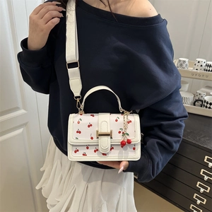 White crossbody square bag with red cherry pattern and golden clasp on a female model