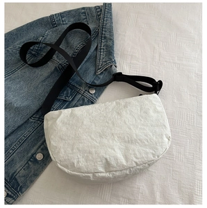 Detail of white textured crossbody bag with black adjustable strap on denim background