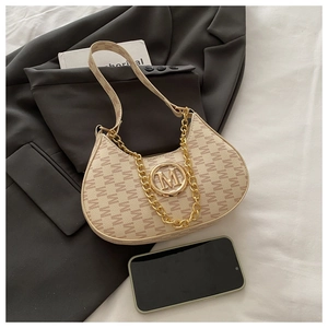 Detail of beige crescent moon bag with golden M logo and chunky chain on a grey blazer