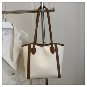 Close-up of minimalist cream leather tote bag with brown straps hanging on a metal rack