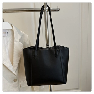 Close-up of a large black leather tote bag with matte texture and minimalist shoulder strap