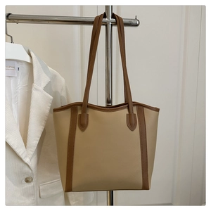 Detail view of large beige tote bag with brown handles hanging in a casual setting