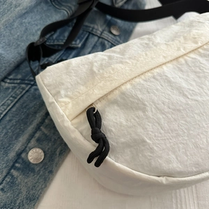 Detail of white textured fabric crossbody bag with black rope zipper puller and strap