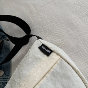 Detail showing white crinkled fabric texture and black strap of the minimalist crossbody bag