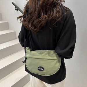 Close-up of bean green crescent crossbody bag with adjustable black strap and logo detail