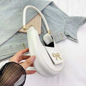 Detail of white textured shoulder bag featuring a decorative gold bow buckle