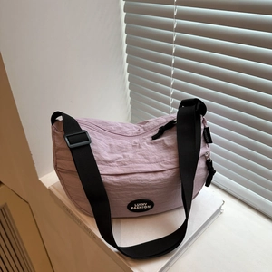 Close-up of lavender nylon crescent bag with adjustable strap on white book background