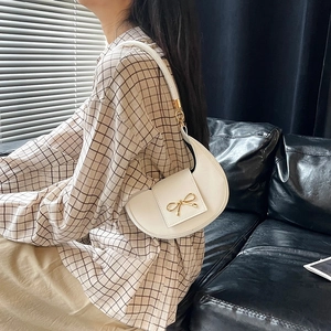 Borsa sottobraccio beige a mezzaluna con fiocco dorato indossata da una modella