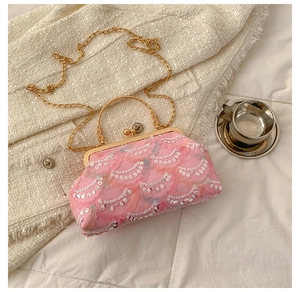 Pink sequin crossbody bag with gold chain strap on elegant tweed fabric backdrop