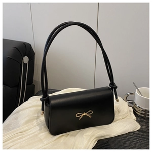 Détail du sac sous l'aisselle noir avec fermoir nœud doré et bandoulières nouées