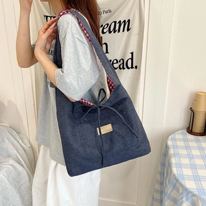 Blue canvas tote bag with bow detail and plaid lining shown on a female model
