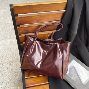 Sac cabas bordeaux brillant avec nœud argenté posé sur un banc en bois pour le style