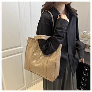 Detail of beige woven texture tote bag worn on shoulder by model in modern room