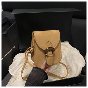 Détail du petit sac bandoulière camel avec boucle en bois sur fond de soie