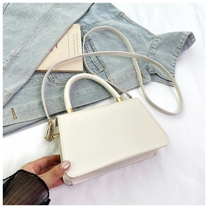 Detail shot of a cream leather handbag with gold hardware and reinforced handle on denim