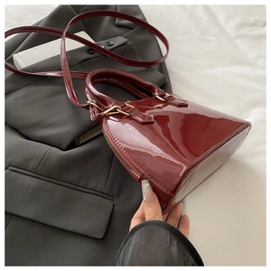 Detail of burgundy patent leather shell bag texture on a grey suit blazer background
